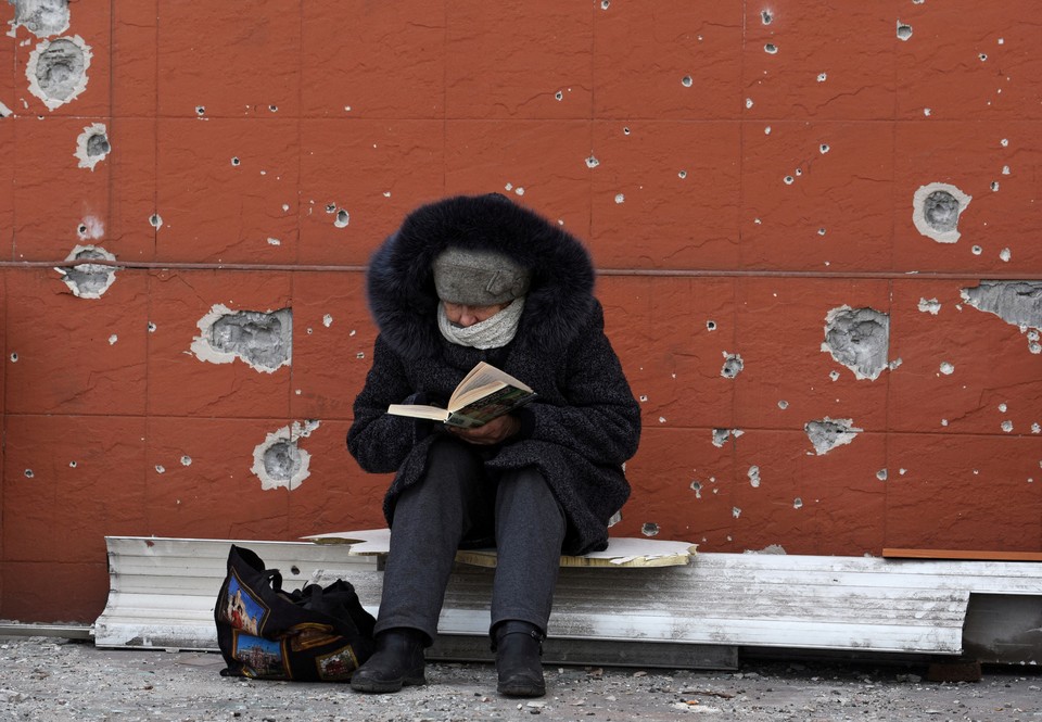 Жительница Мариуполя за чтением книги на фоне стены с последствиями боев